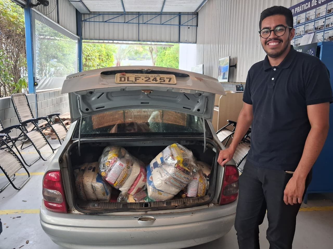 Homem está perto de um porta-malas de carro cheio de sacos de comida, provavelmente para doação.