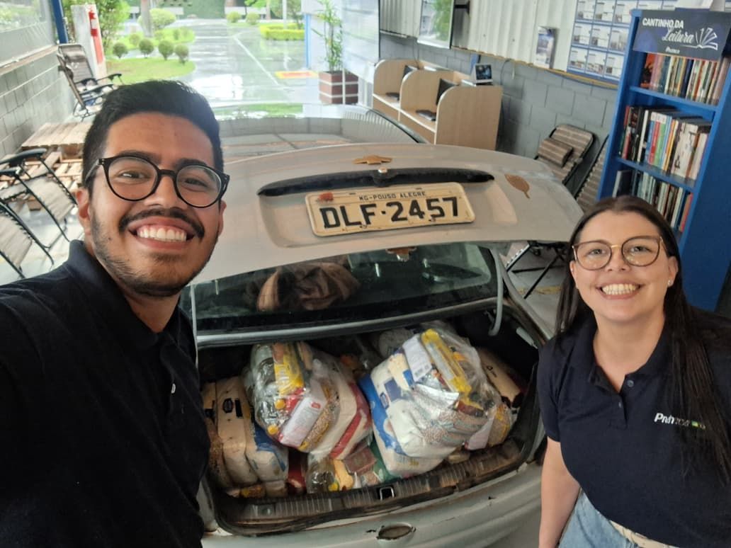 Duas pessoas sorrindo perto de um porta-malas de carro cheio de sacolas de suprimentos.