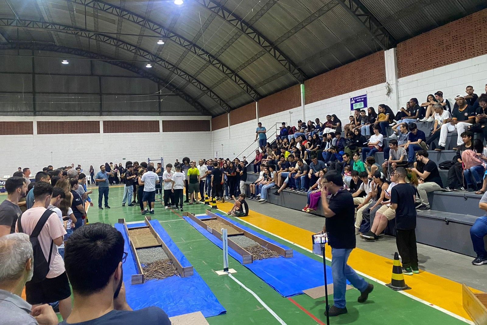 Um grande grupo de pessoas está em um ginásio assistindo a um jogo.