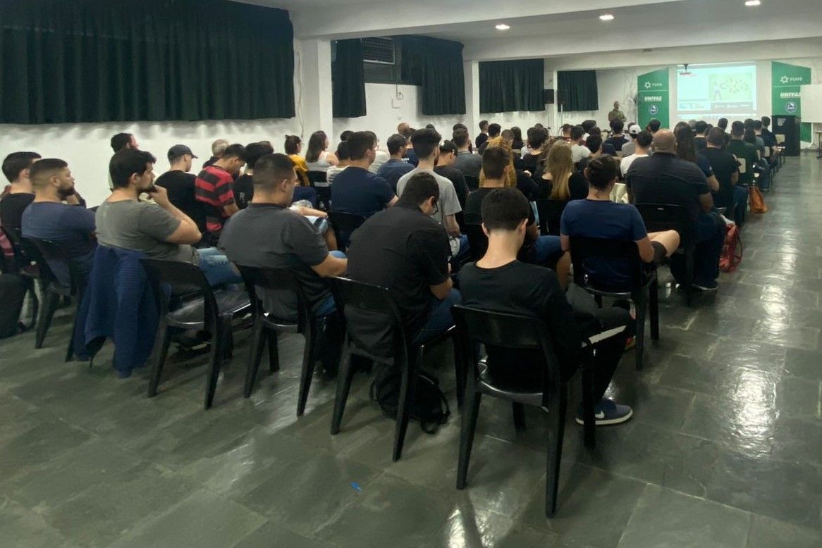 Um grande grupo de pessoas está sentado em cadeiras em uma sala.