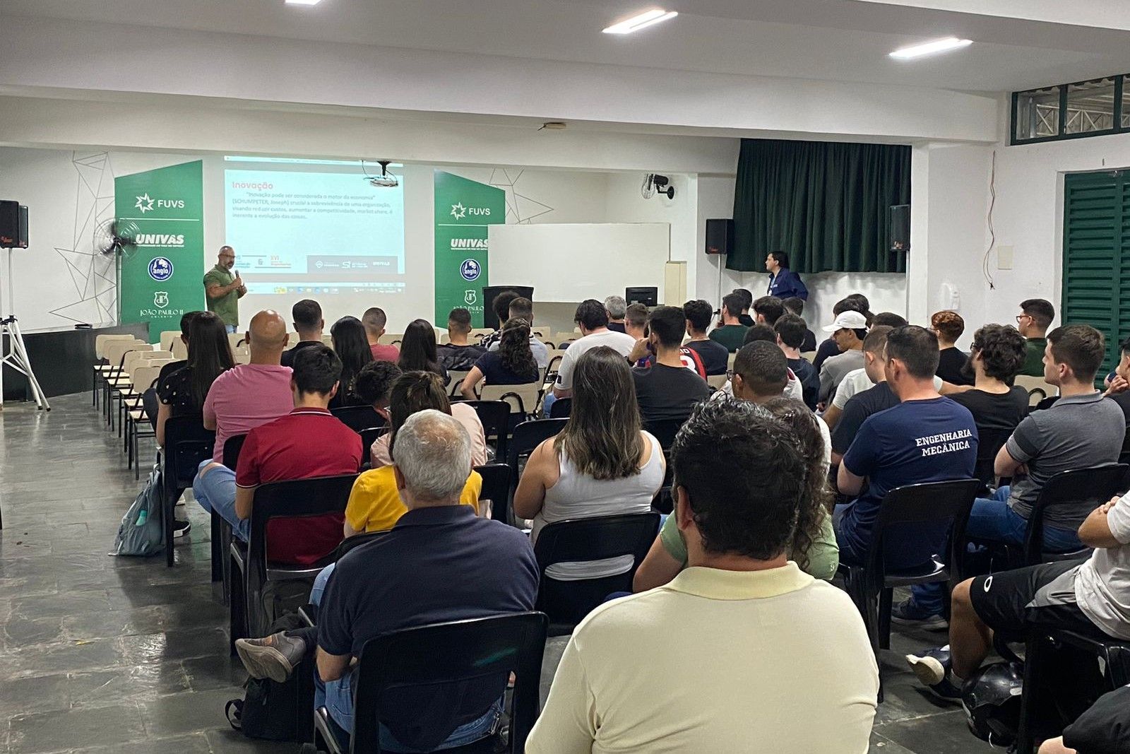 Um grupo de pessoas está sentado em cadeiras em frente a uma tela de projetor.