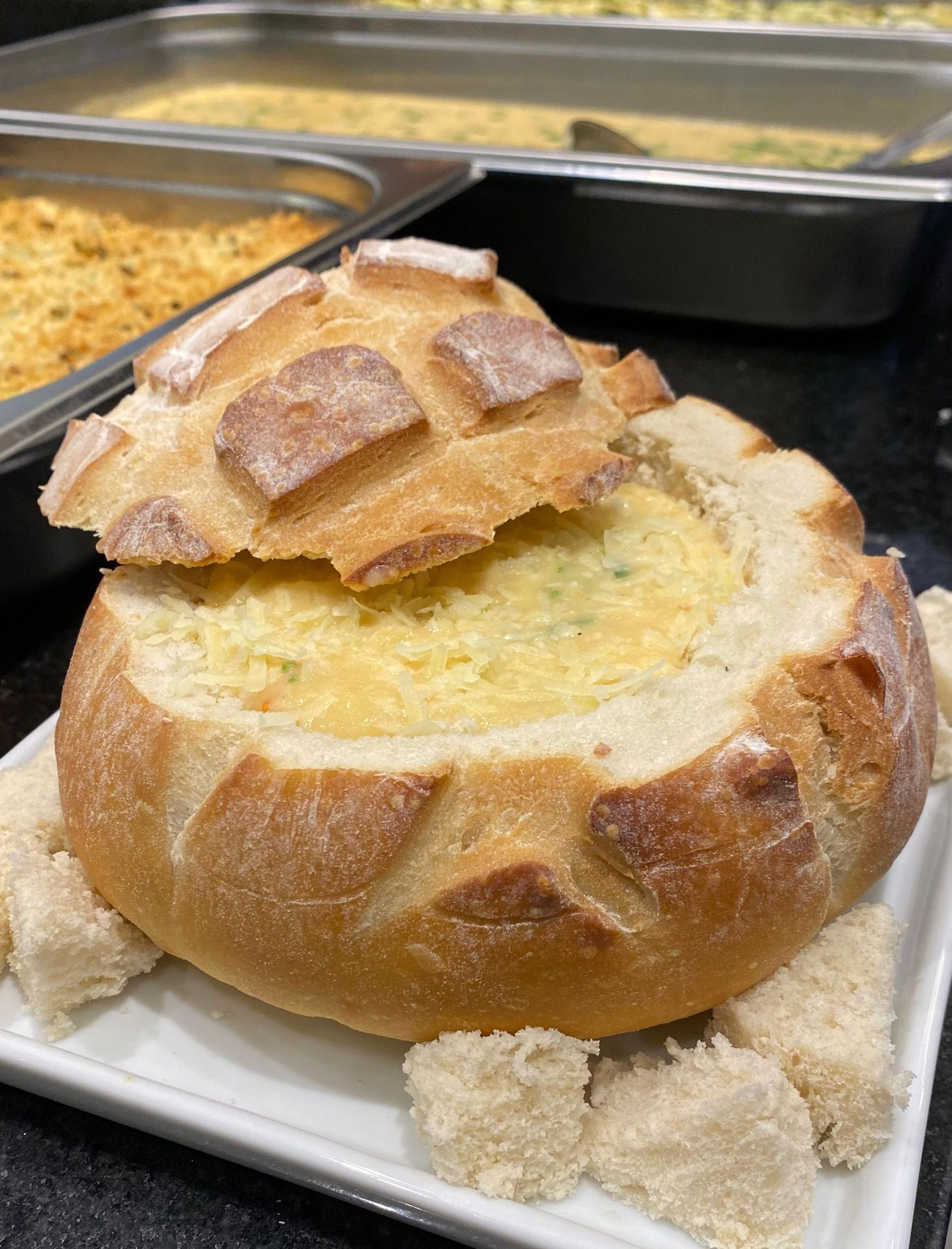 Uma tigela de sopa dentro de um pão em um prato.