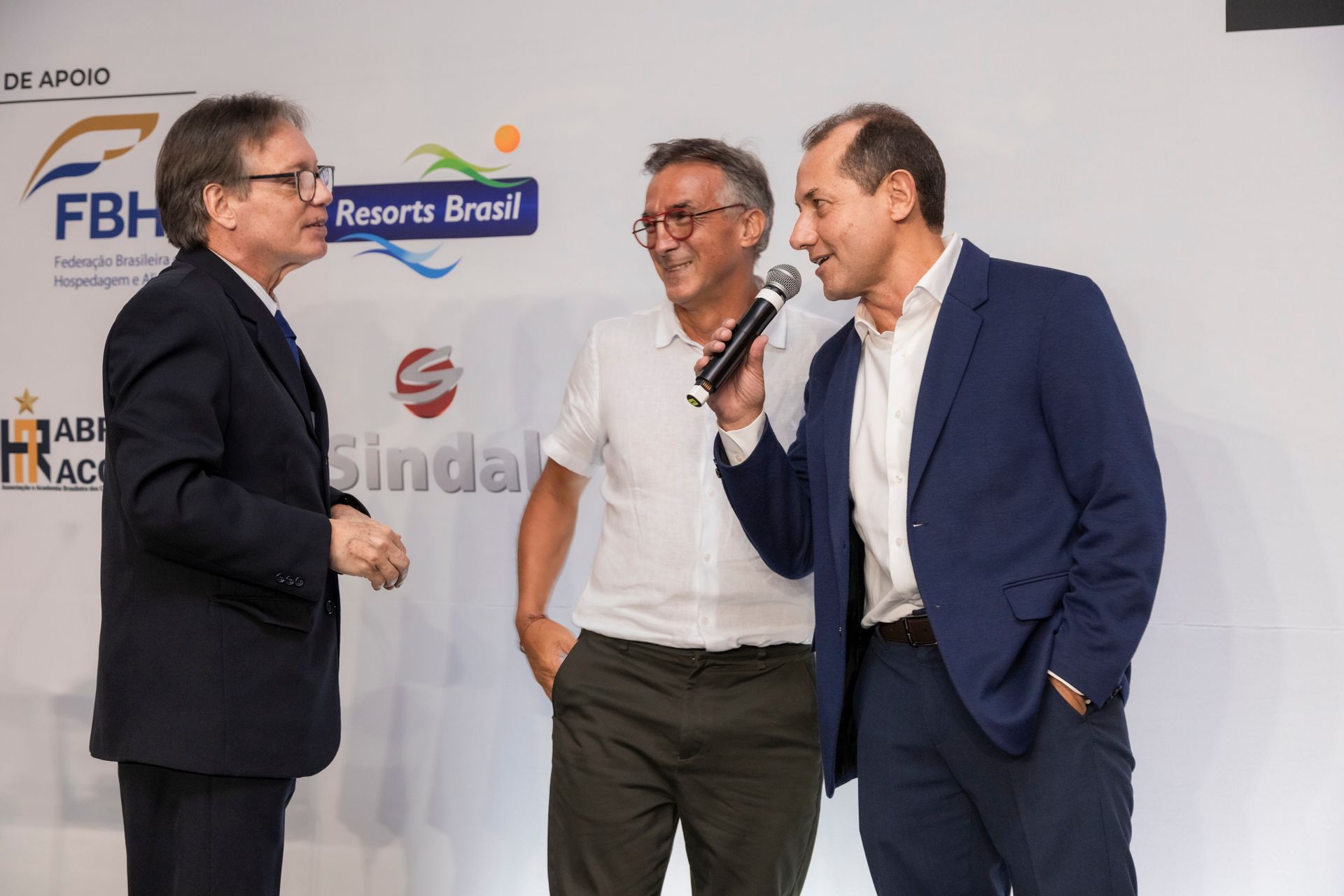 Três homens estão de pé um ao lado do outro e um deles está segurando um microfone.