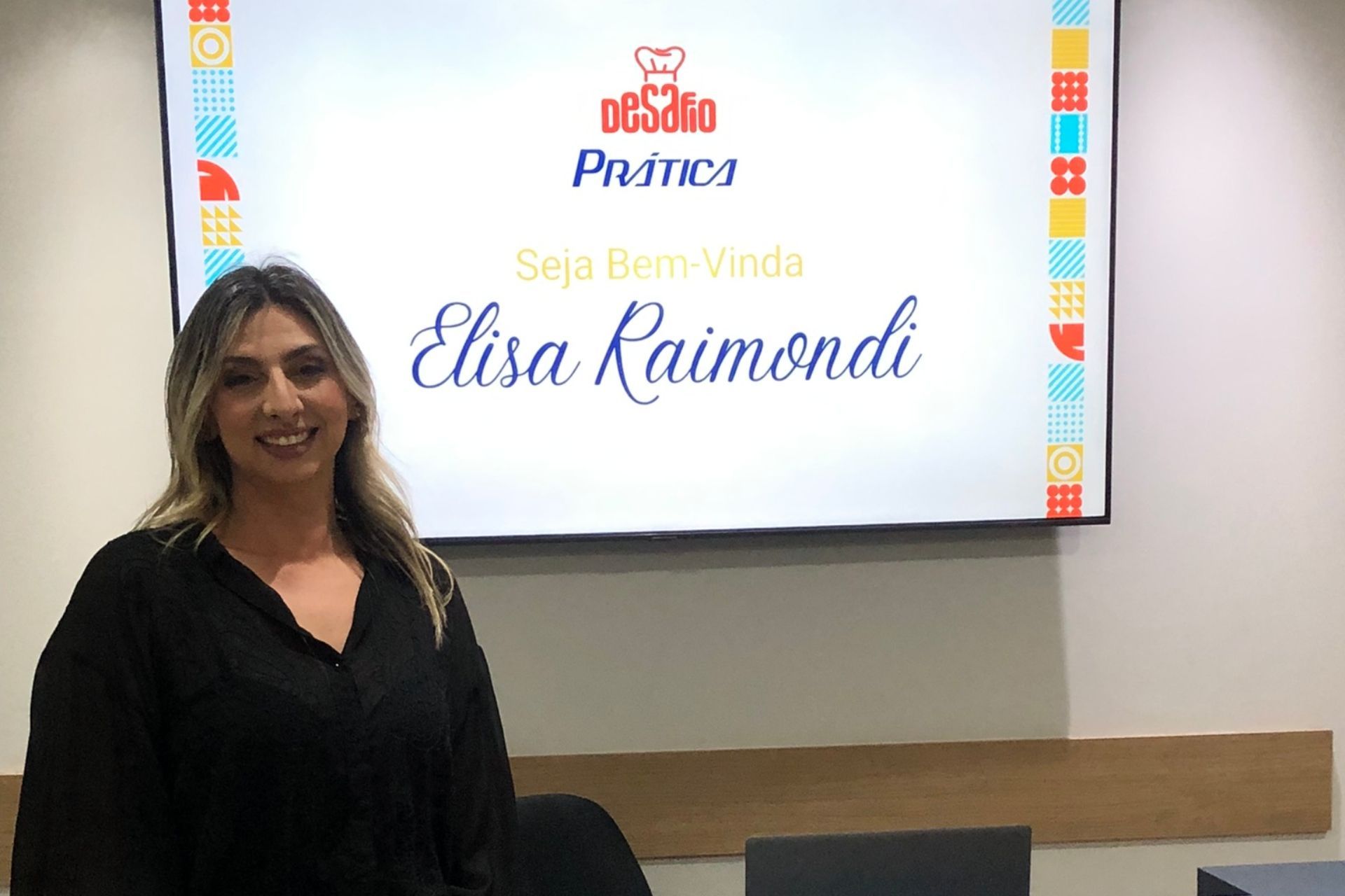 Mulher sorrindo em frente a uma tela que exibe 