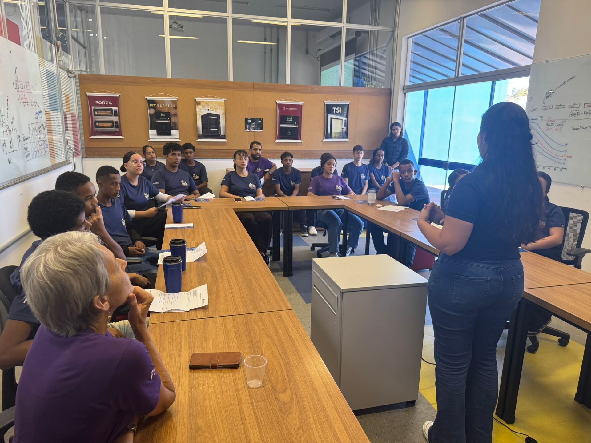 Uma mulher falando para um grupo de pessoas sentadas ao redor de uma mesa em uma sala de conferências.