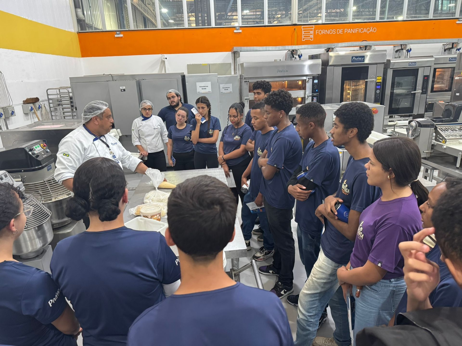 Chef demonstrando como fazer pão para alunos em uma cozinha profissional.