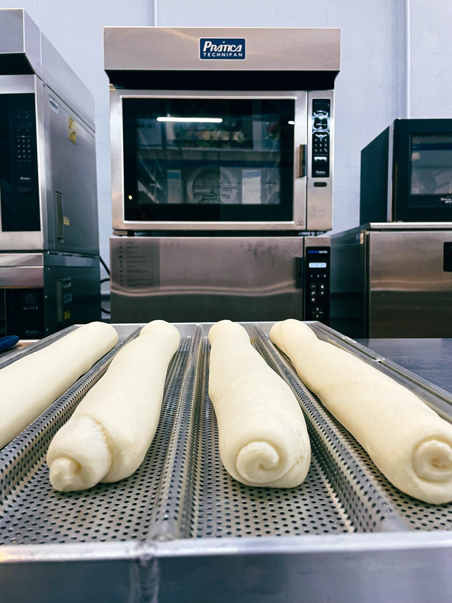 Rolos de massa estão em uma bandeja em frente a um forno a gás