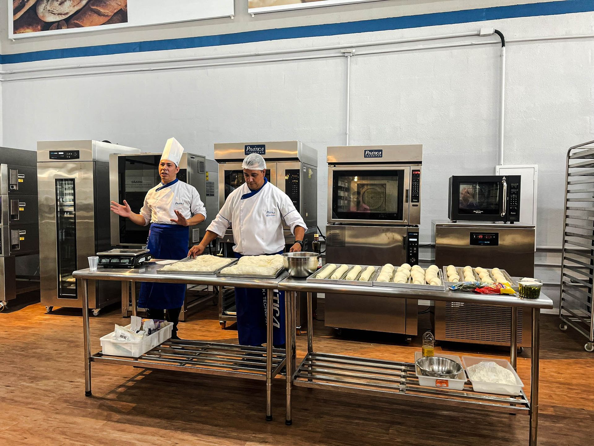Dois chefs estão em pé em uma mesa na cozinha.