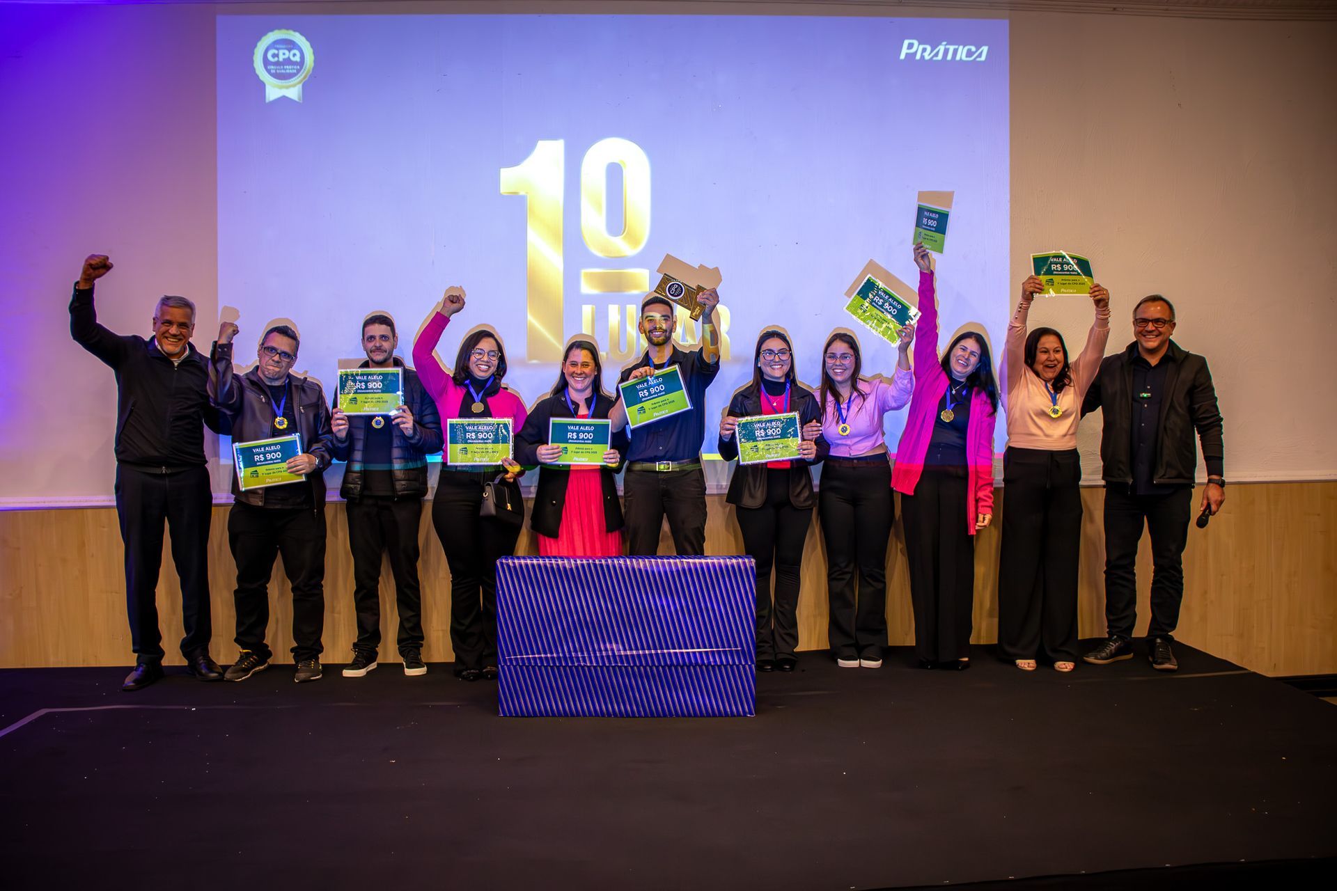 Grupo de pessoas no palco segurando certificados, comemorando um marco de 10 anos com detalhes em azul e verde.