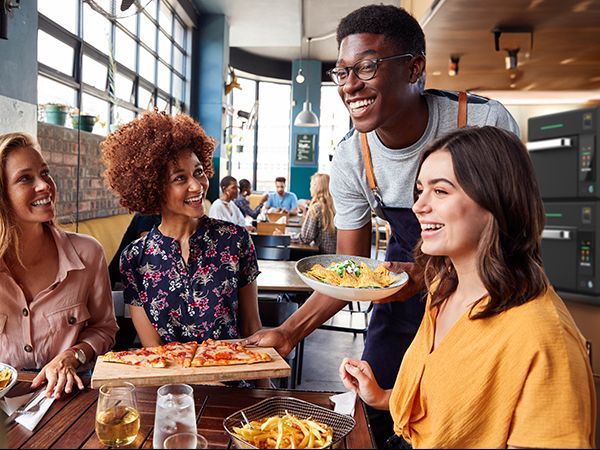 Um garçom está servindo comida para um grupo de pessoas em um restaurante.