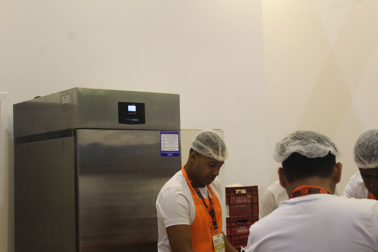 Um grupo de homens trabalha em uma cozinha em frente a uma geladeira.