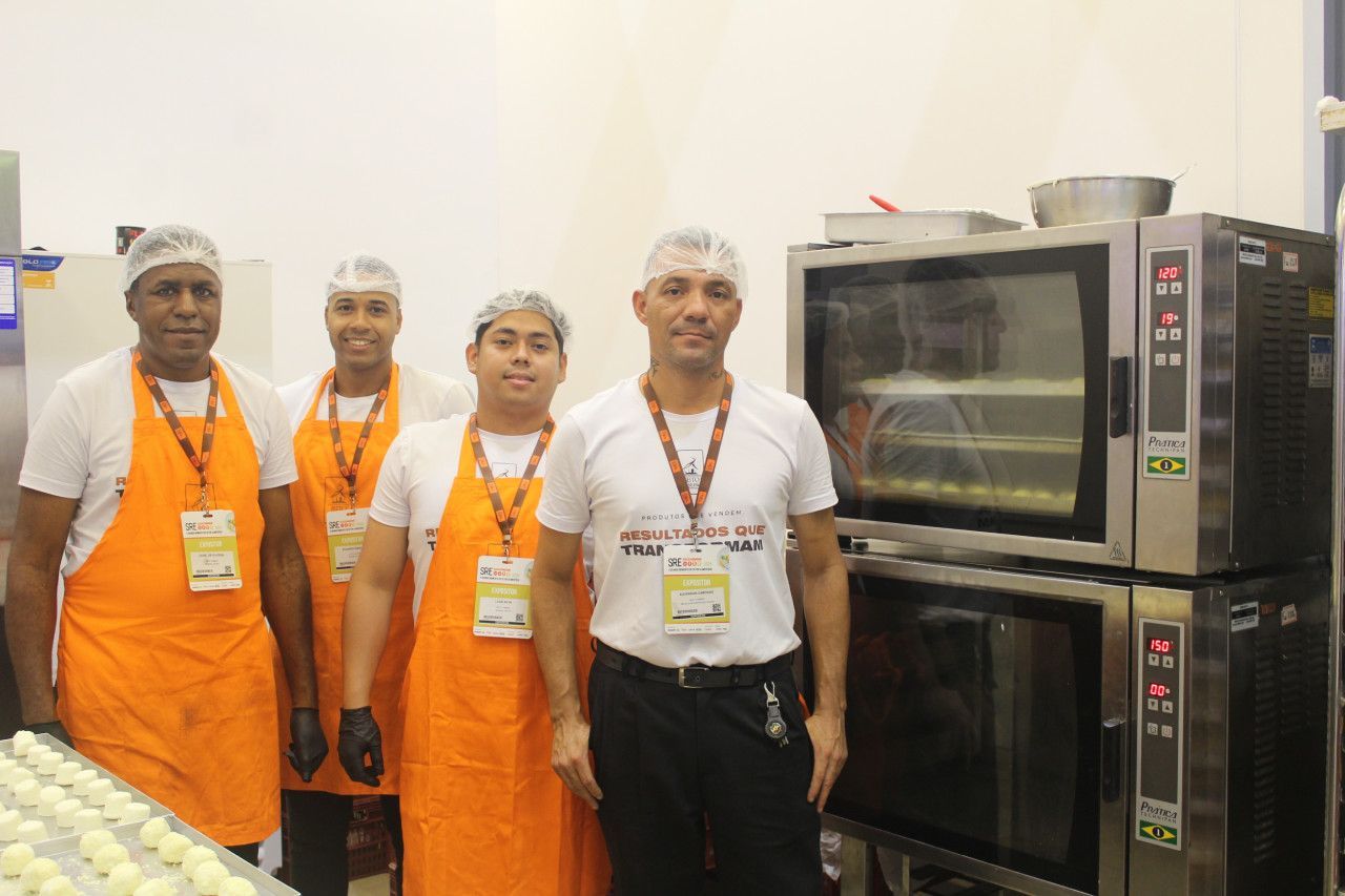 Um grupo de chefs posa para uma foto em frente a uma pilha de fornos.