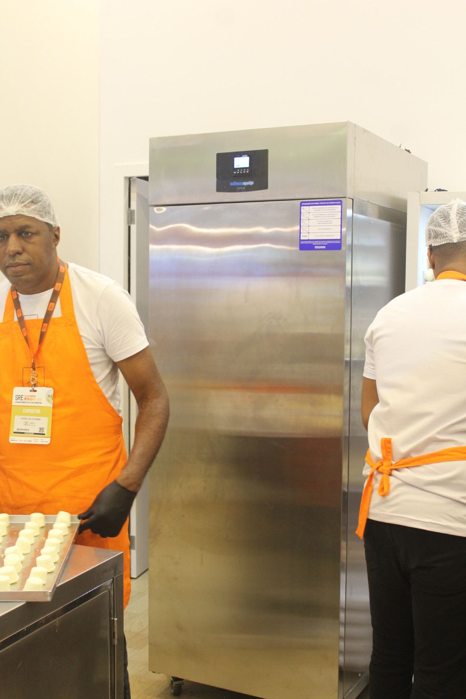 Um homem com um avental laranja está parado em frente a uma geladeira de aço inoxidável