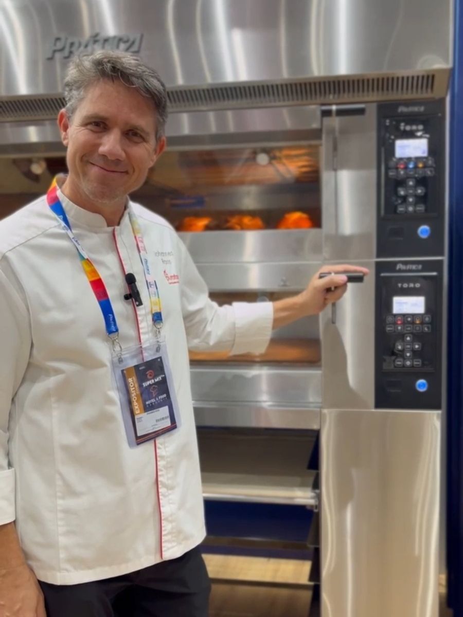 Um homem com uniforme de chef está parado em frente a um forno.