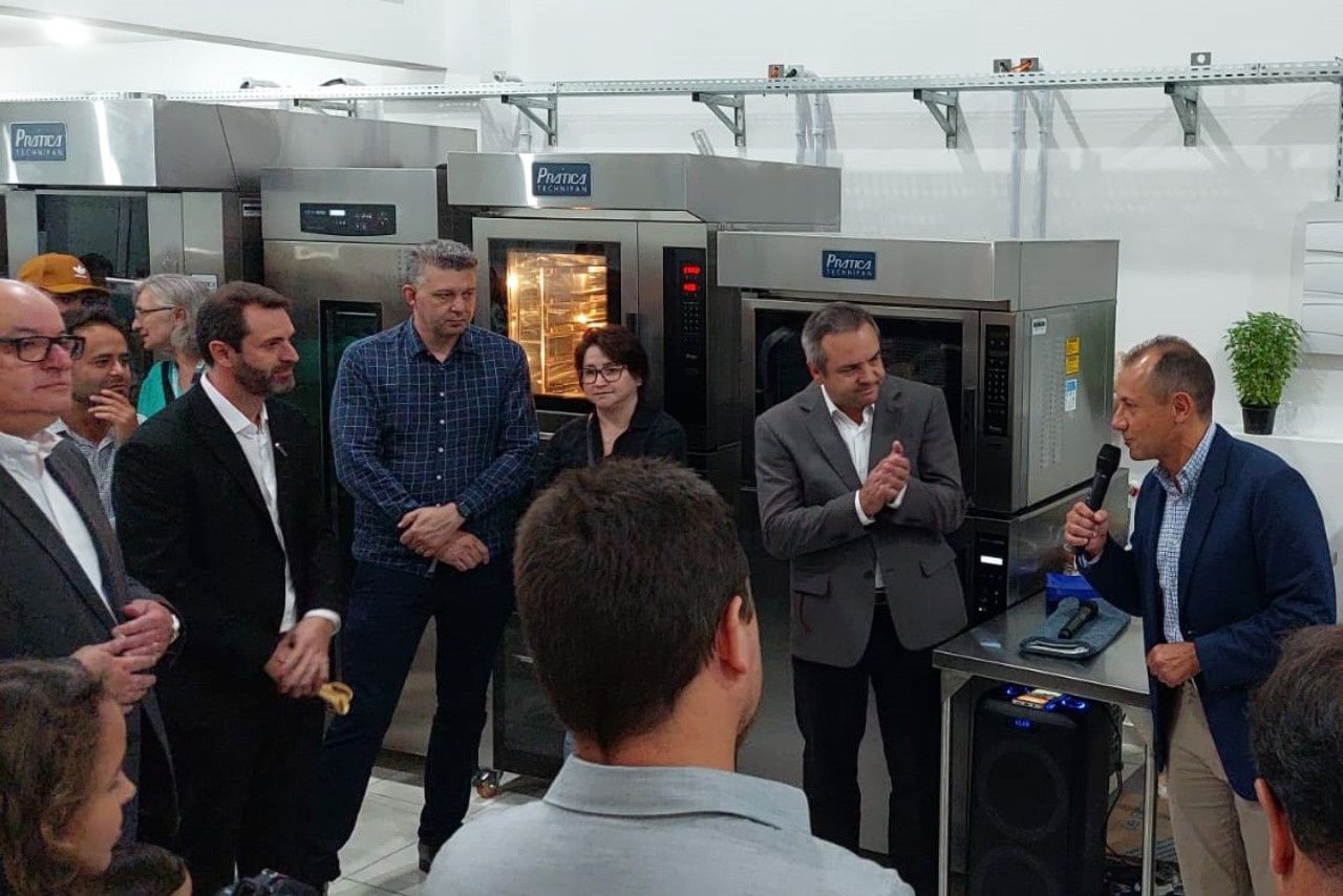 Um grupo de pessoas está em frente a um microfone em uma cozinha.