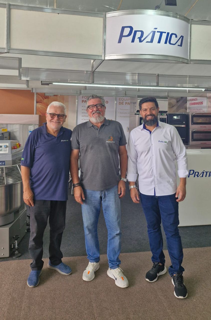 Três homens estão posando para uma foto em frente a uma placa que diz pratica.
