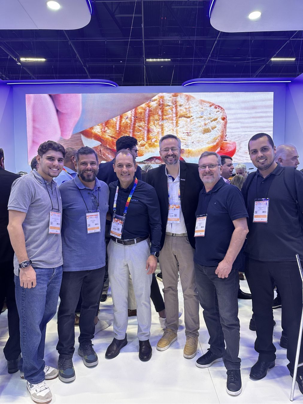 Um grupo de homens está posando para uma foto em frente a uma tela grande.