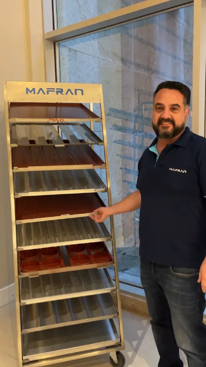 Um homem de camisa azul está parado ao lado de um carrinho com bandejas.