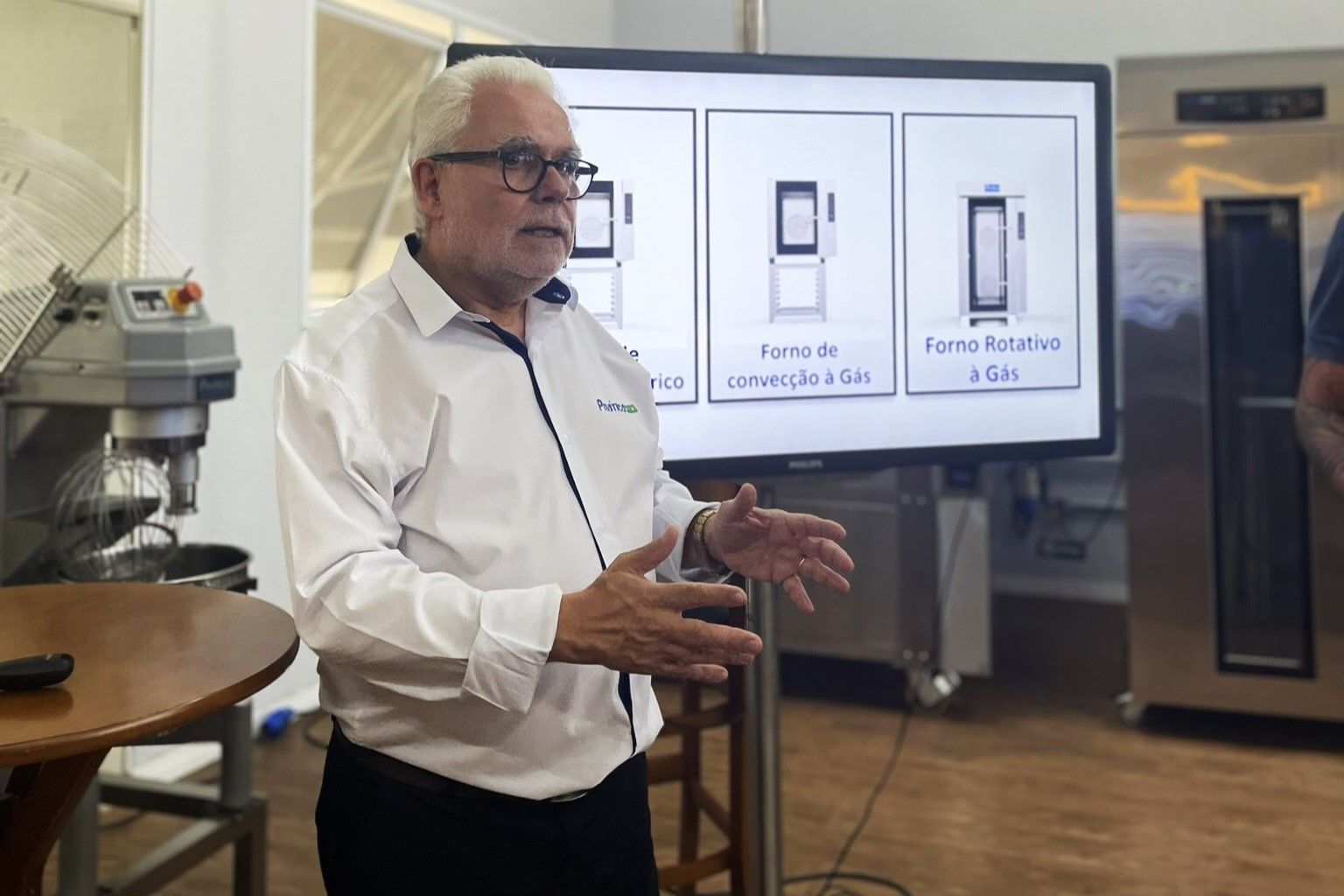 Um homem de camisa branca está parado em frente a uma tela grande.