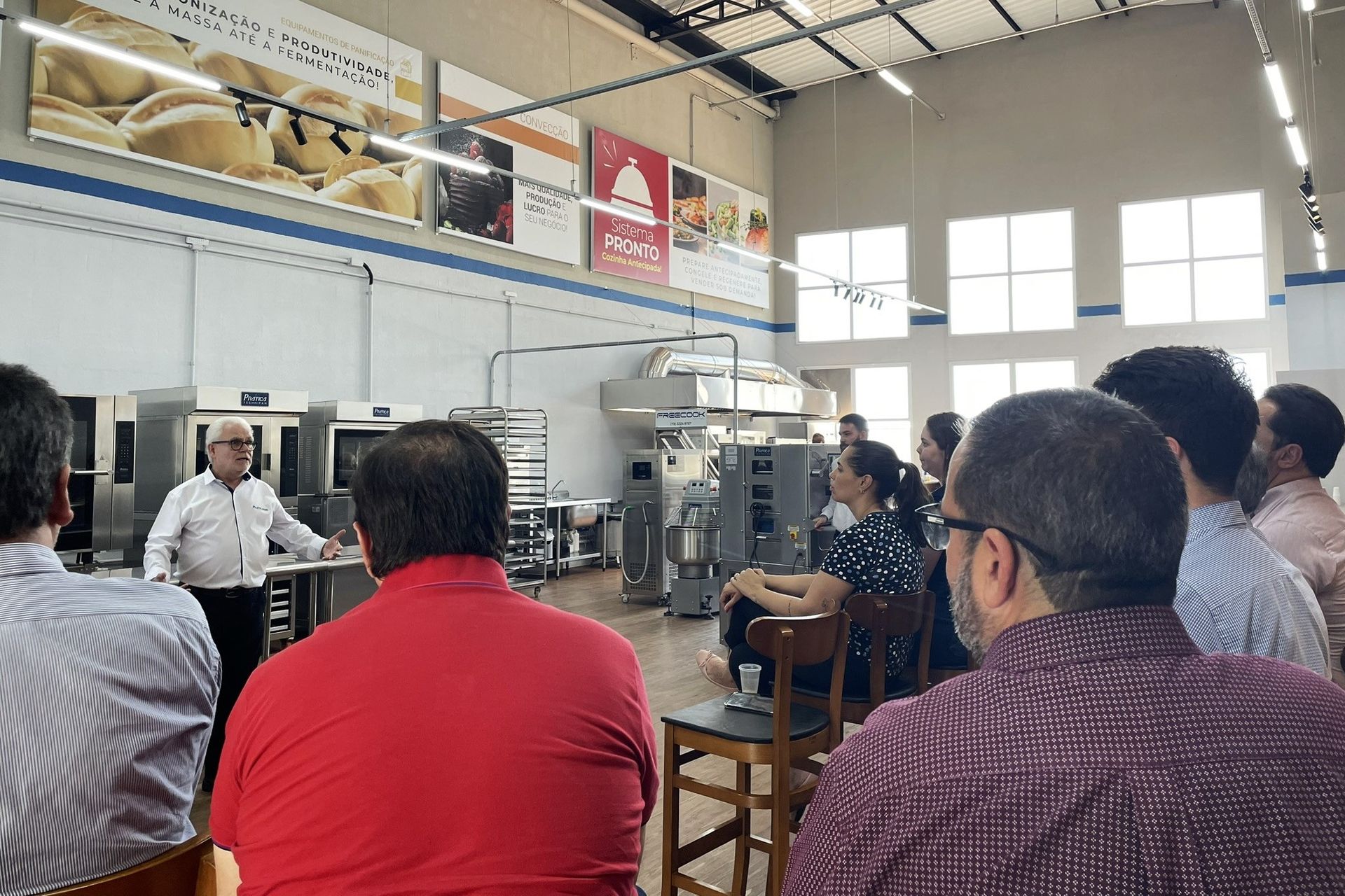 Um grupo de pessoas está sentado em uma sala com um homem fazendo uma apresentação.