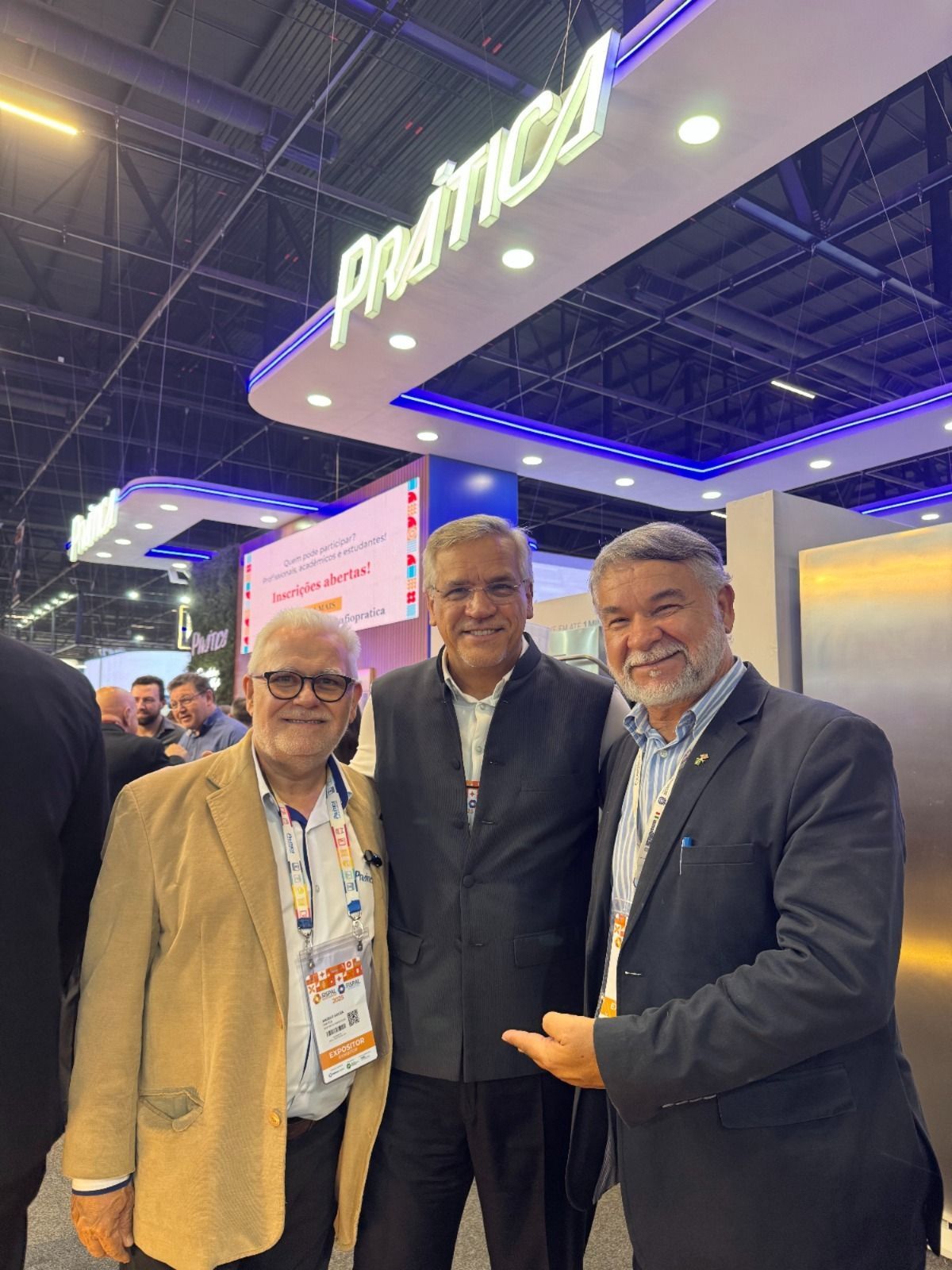Três homens estão posando para uma foto em frente a uma placa que diz andmed.