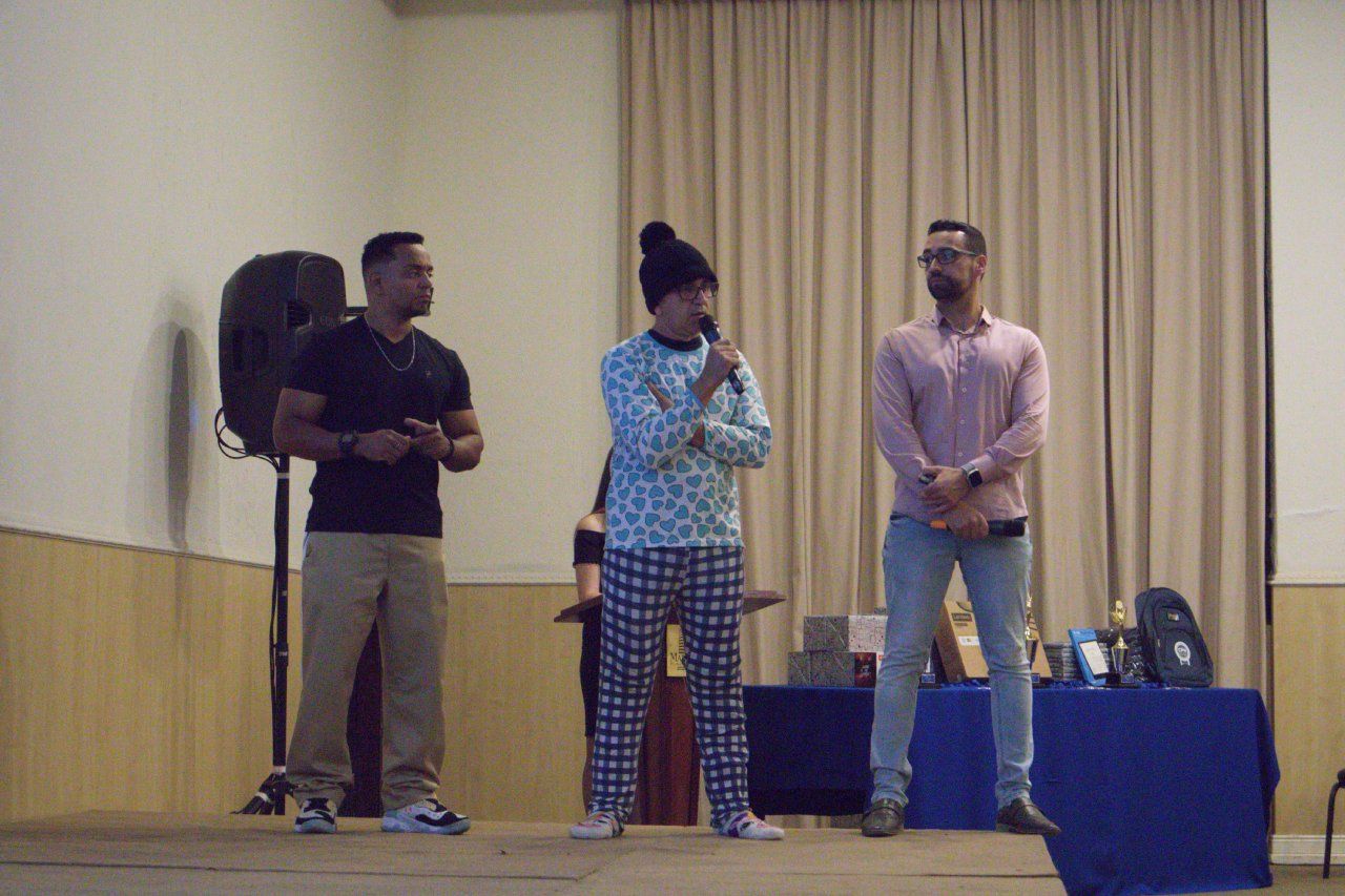 Três homens estão em pé em frente a um microfone em uma sala.