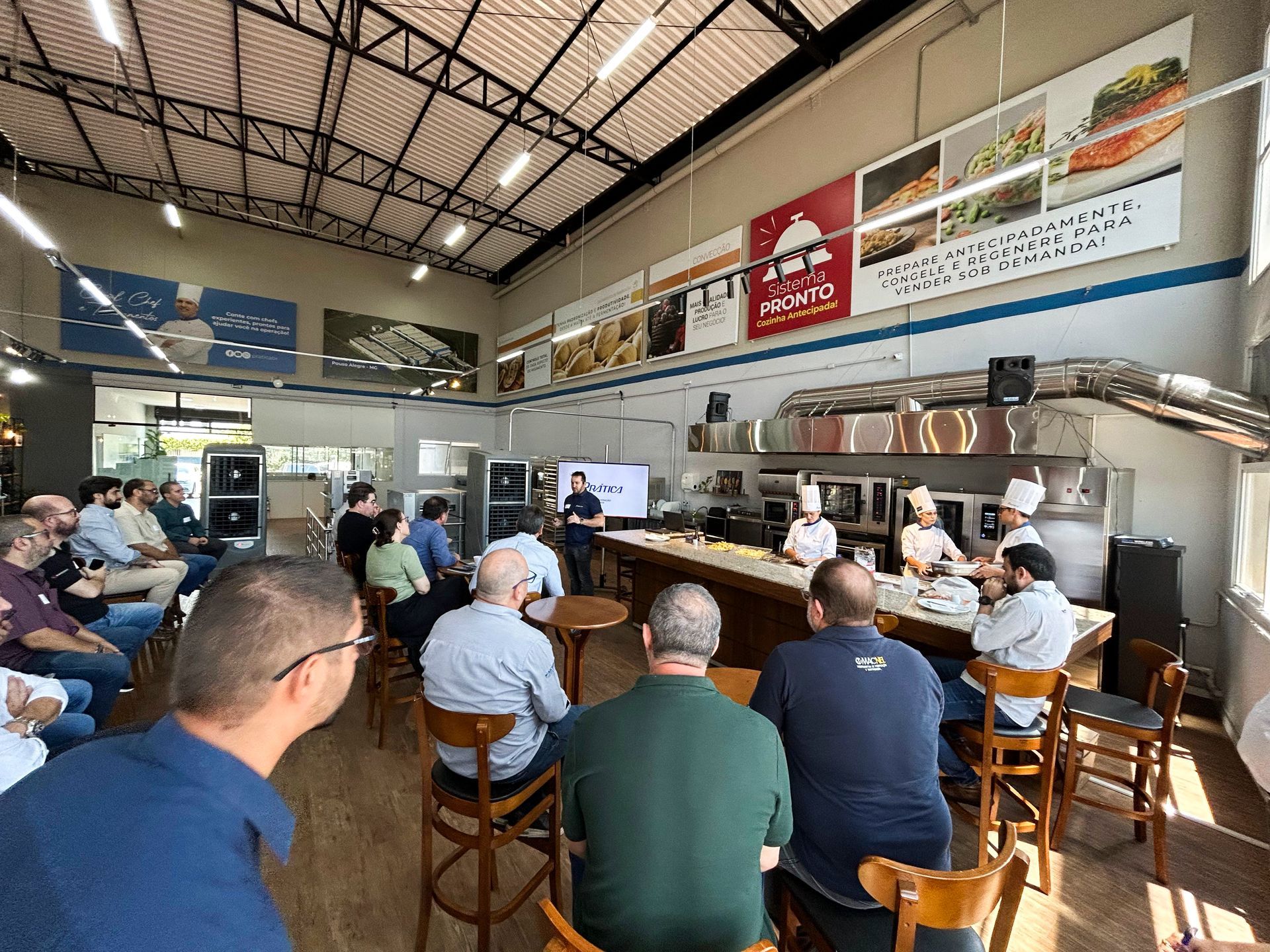 Um grupo de pessoas está sentado em mesas em um restaurante assistindo a uma apresentação.