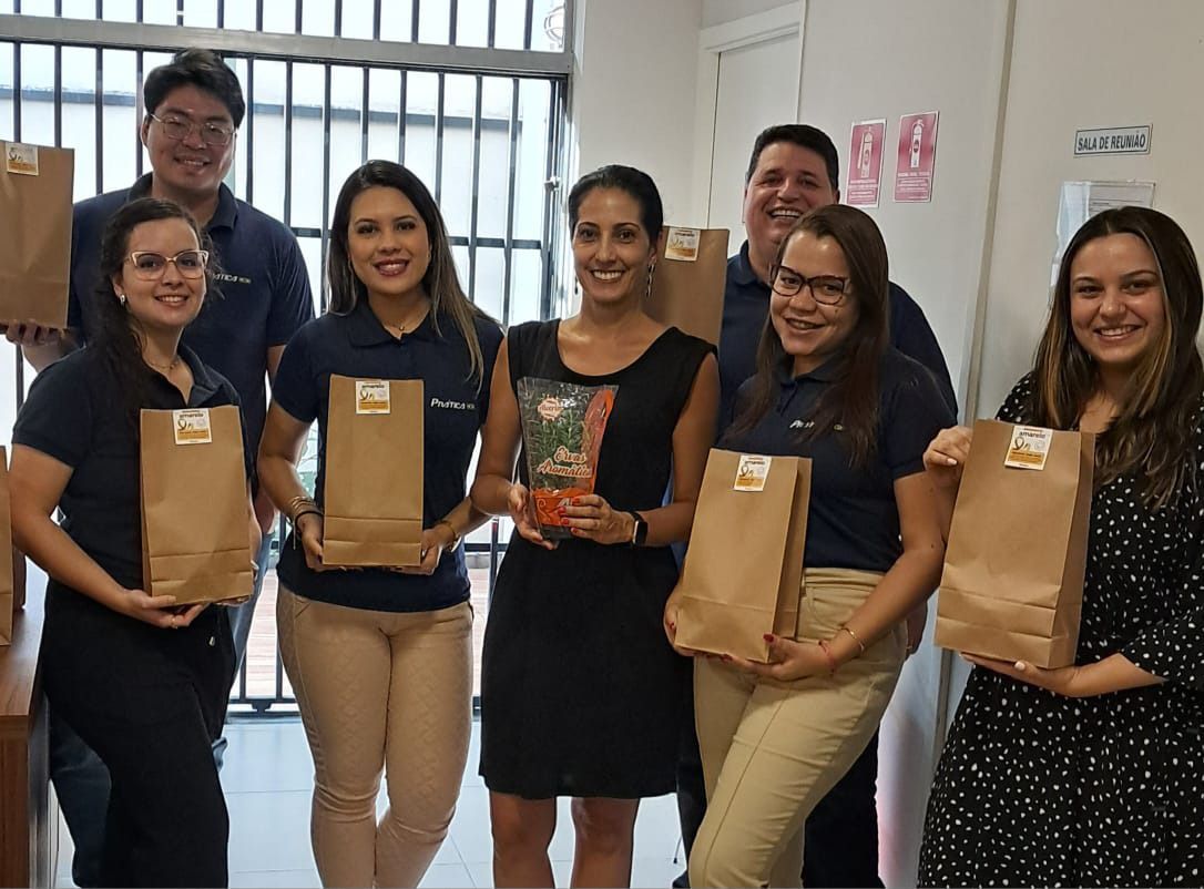 Um grupo de pessoas está de pé, uma ao lado da outra, segurando sacolas marrons.