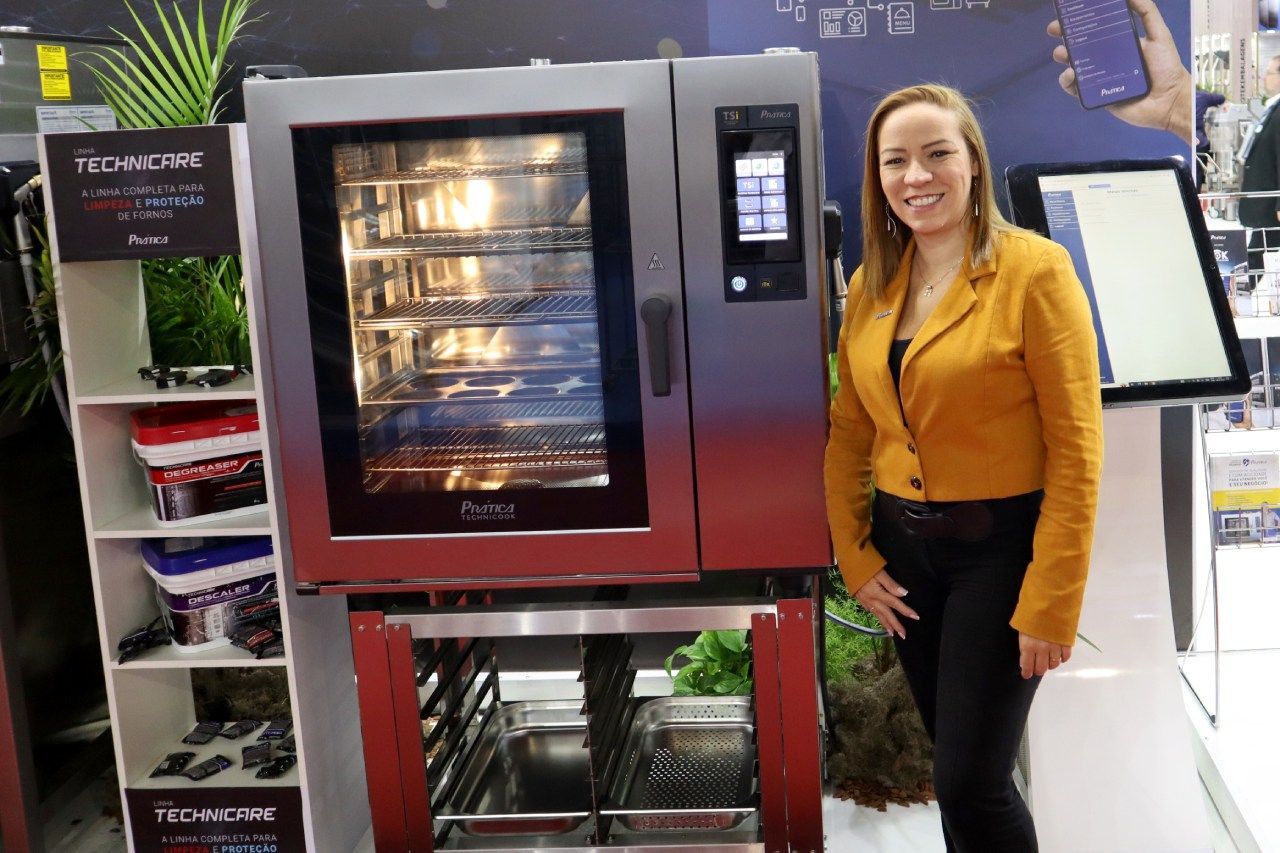 Uma mulher com uma jaqueta amarela está parada em frente a um forno.