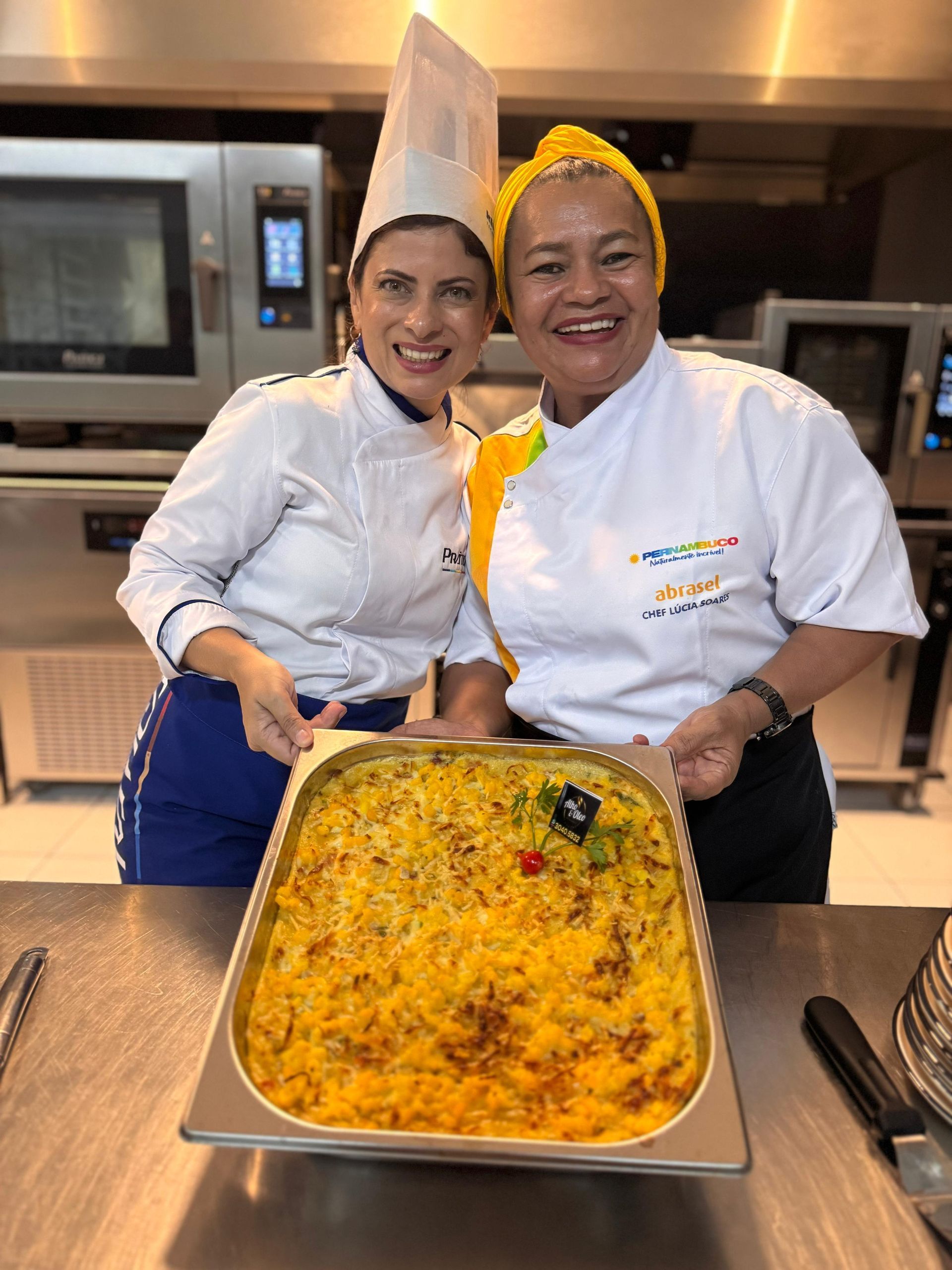Duas mulheres estão de pé, uma ao lado da outra, segurando uma bandeja de comida.