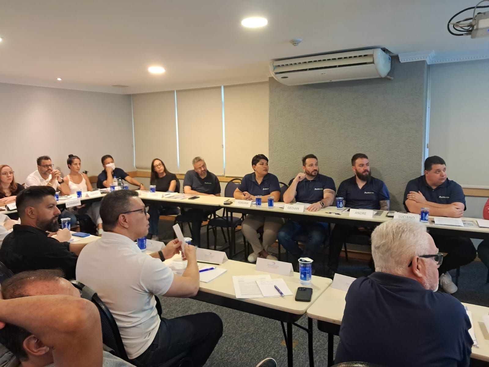 Um grupo de pessoas está sentado em mesas em uma sala de conferências.