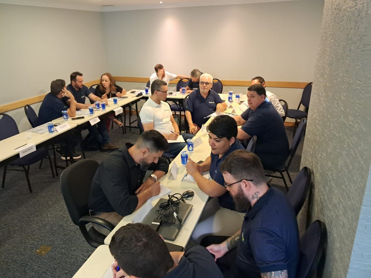 Um grupo de pessoas está sentado ao redor de mesas em uma sala.