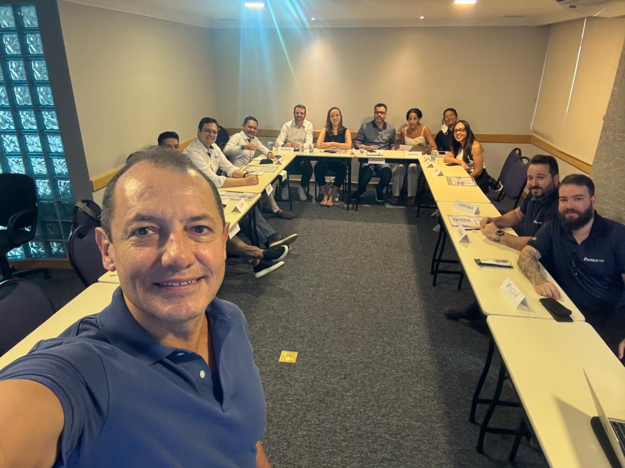 Um homem está tirando uma selfie na frente de um grupo de pessoas sentadas em mesas compridas