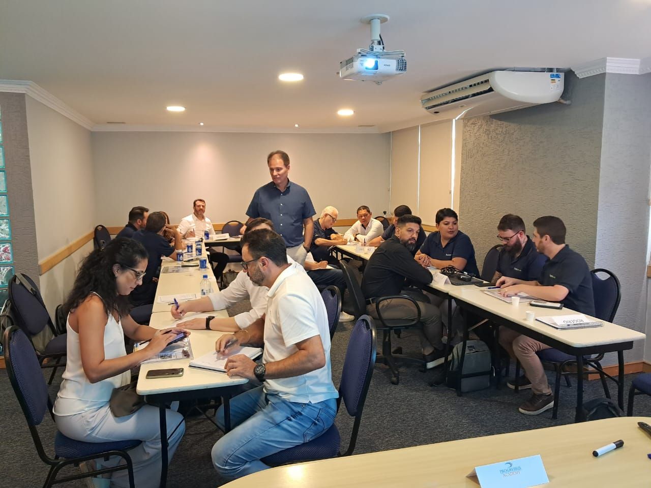 Um grupo de pessoas está sentado em mesas em uma sala de conferências.