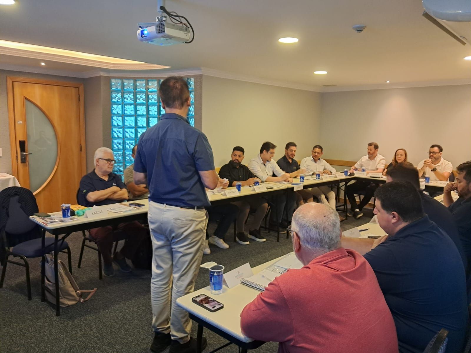 Um homem está fazendo uma apresentação para um grupo de pessoas sentadas em mesas em uma sala.