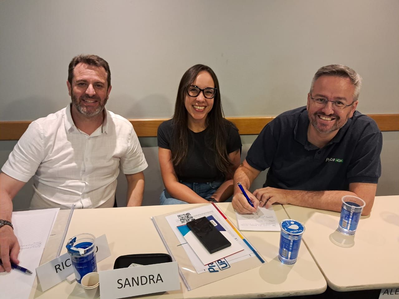 Três pessoas estão sentadas em uma mesa com um crachá que diz sandra.