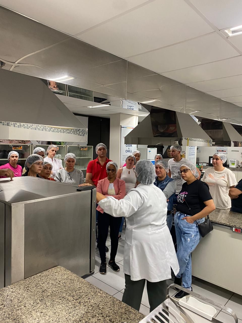 Um grupo de pessoas está em volta de uma mulher na cozinha.