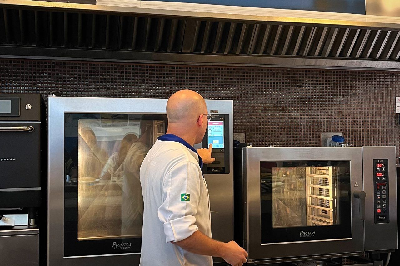 Um homem está diante de um grande forno em uma cozinha.