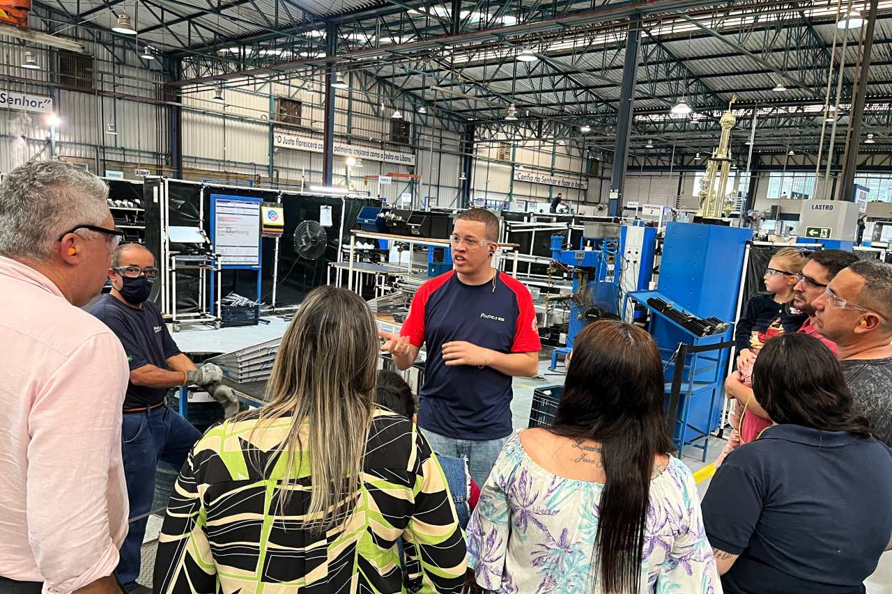 Um grupo de pessoas está ao redor de um homem em uma fábrica.