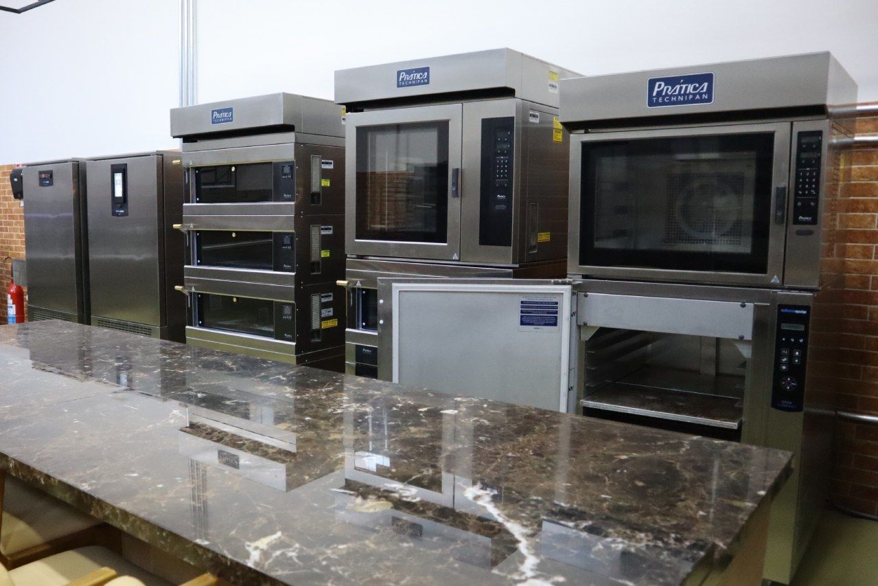 Uma fileira de fornos comerciais estão alinhados um ao lado do outro em um balcão.