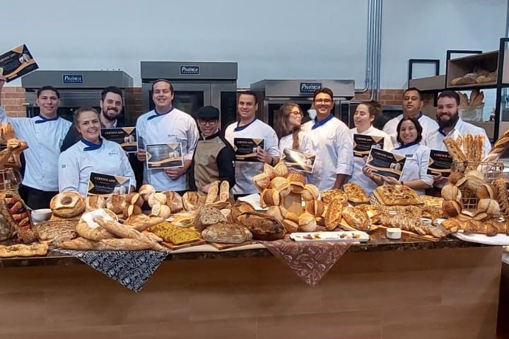 Um grupo de pessoas em pé ao redor de uma mesa cheia de pão.