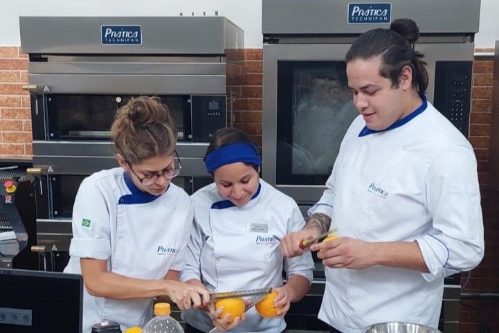 Um homem e duas mulheres estão descascando laranjas em uma cozinha.