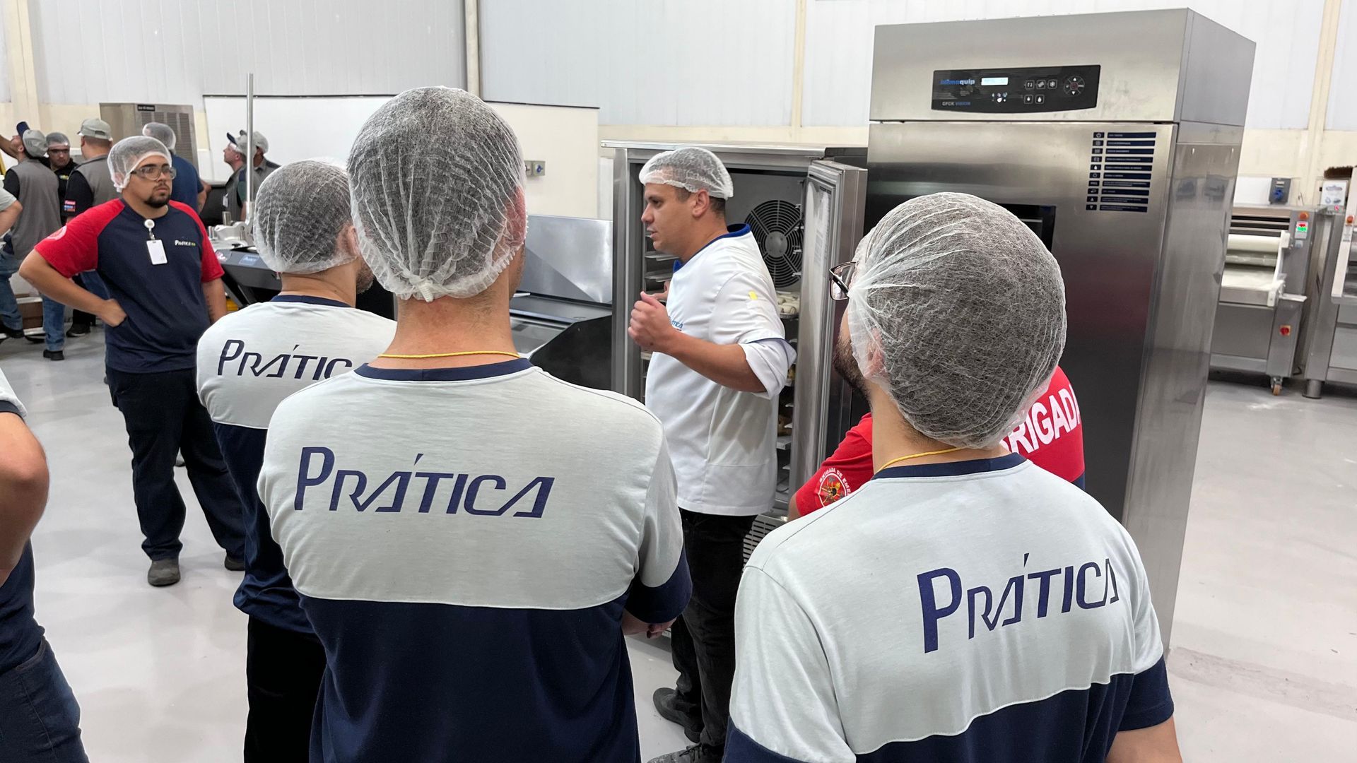 Um grupo de pessoas usando chapéus e camisas de plástico estão em uma cozinha.
