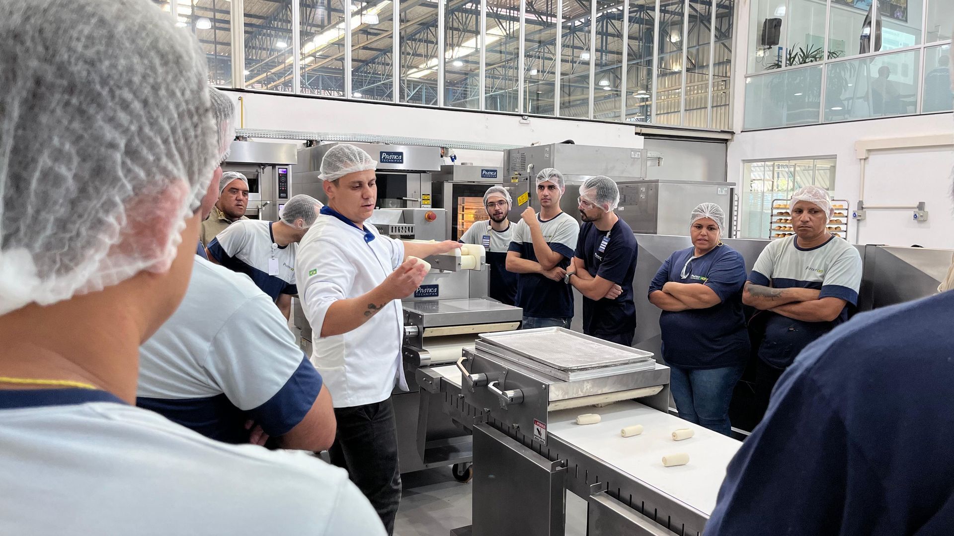 Um homem está fazendo uma apresentação para um grupo de pessoas em uma padaria.