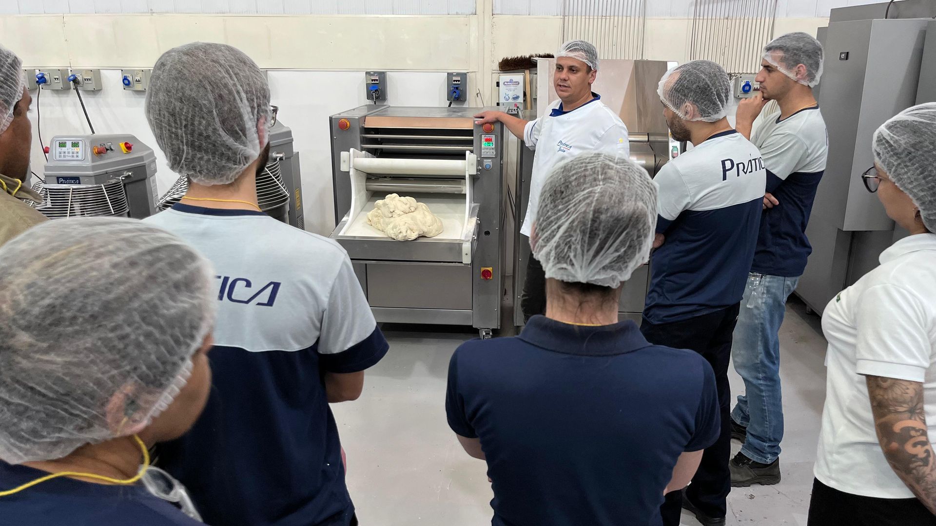 Um grupo de pessoas usando luvas de plástico e redes de cabelo estão em uma cozinha.