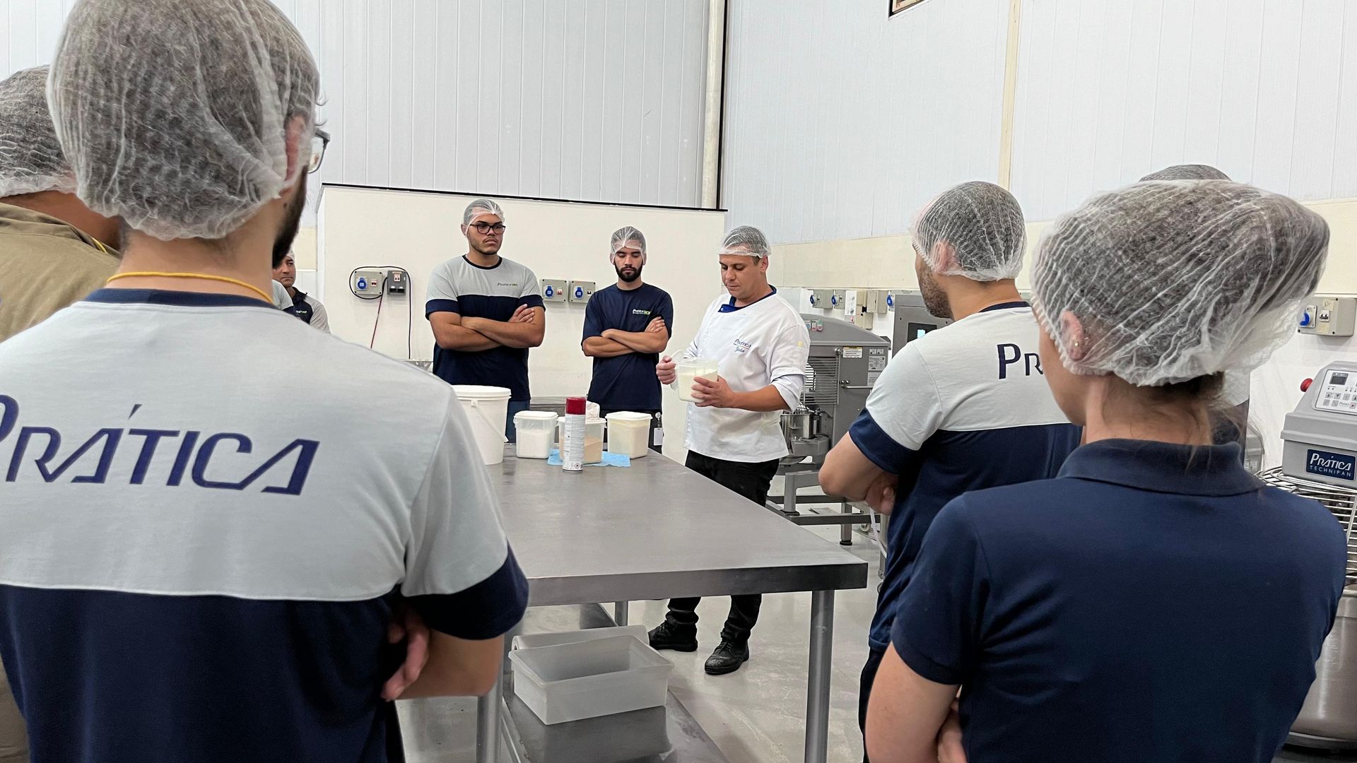 Um grupo de pessoas usando redes de cabelo estão em pé ao redor de uma mesa na cozinha.