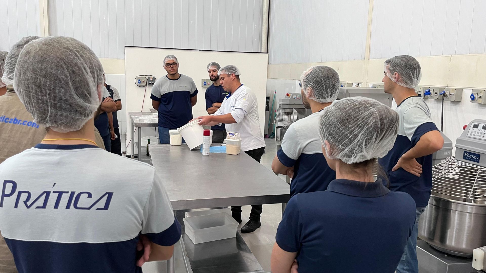 Um grupo de pessoas usando redes de cabelo estão em pé ao redor de uma mesa na cozinha.