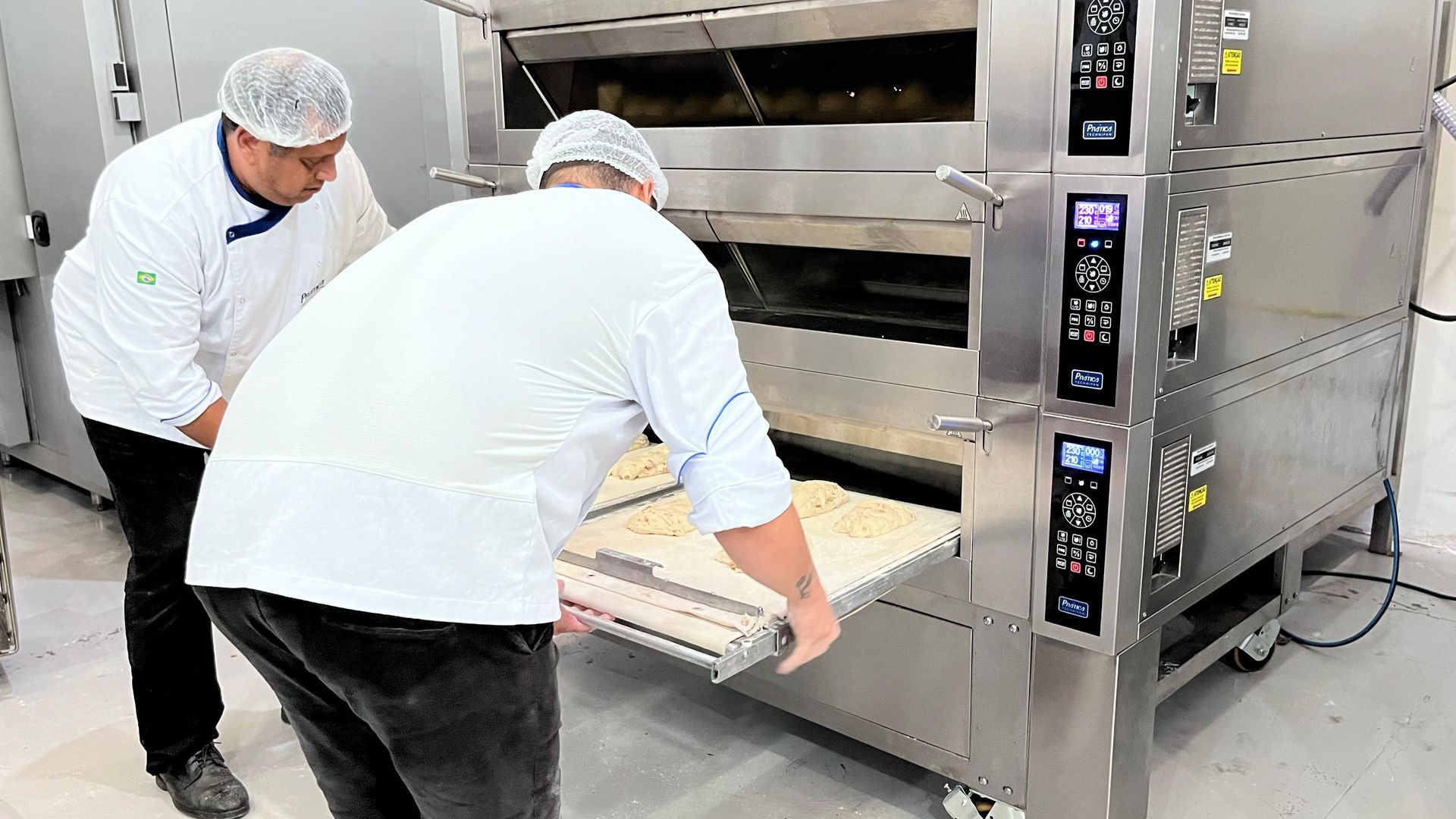 Dois homens estão trabalhando em uma padaria em frente a um forno.