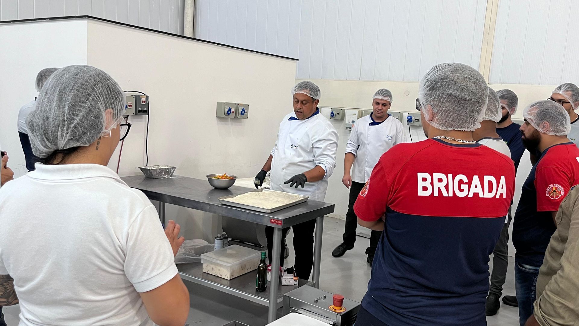 Um grupo de pessoas está em pé ao redor de uma mesa na cozinha.