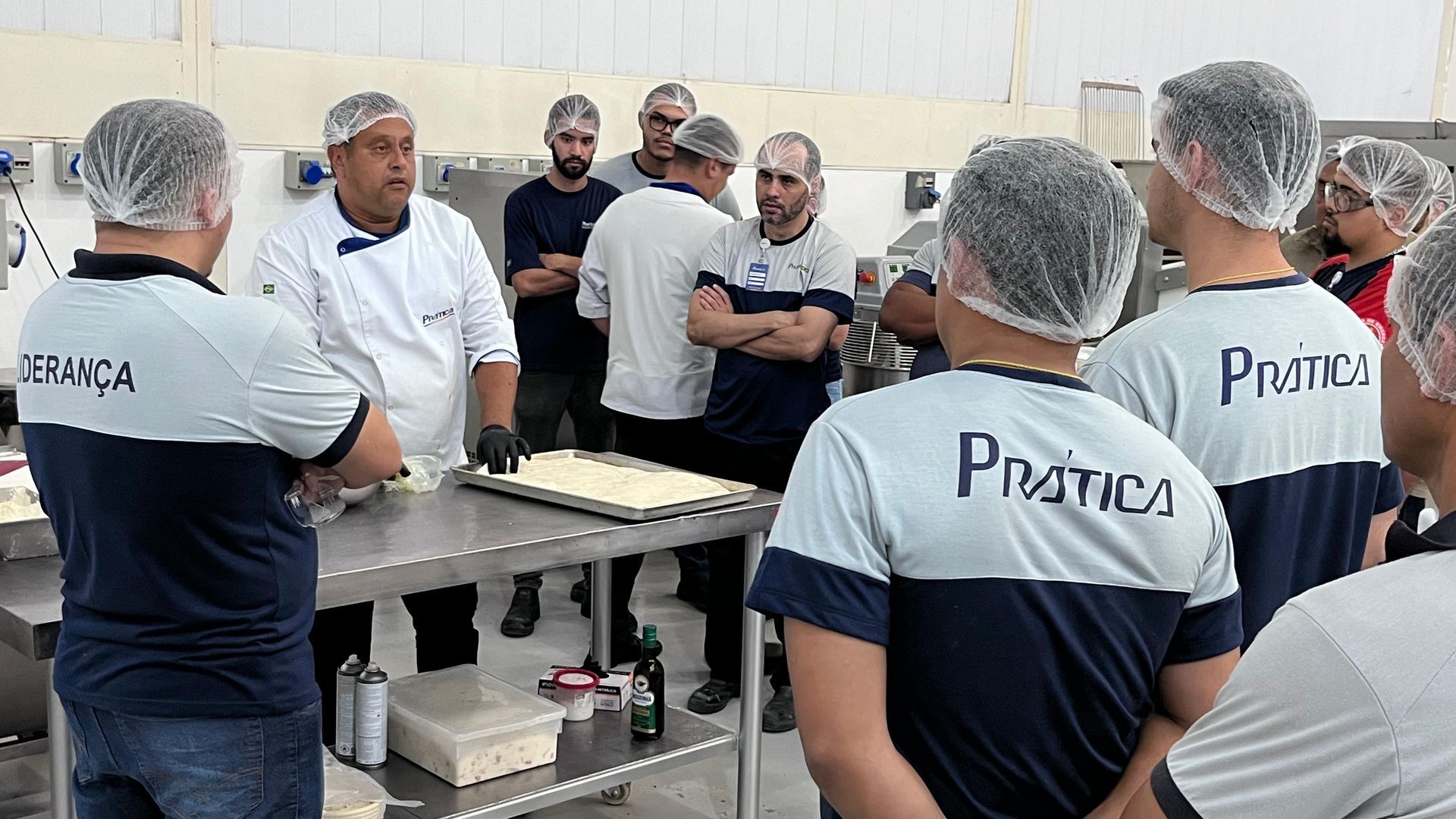 Um grupo de homens está em uma cozinha usando chapéus de plástico e camisas com a palavra pratica nas costas.